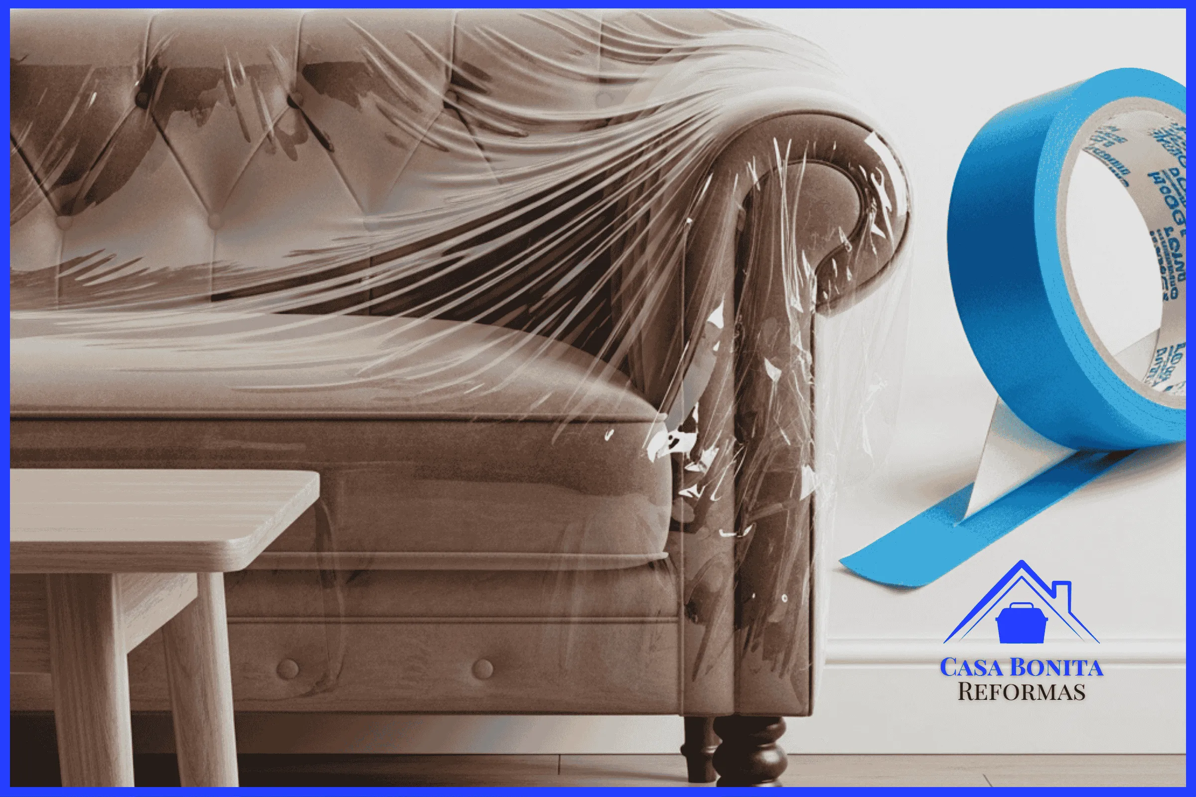 O Envelopamento Eletrostático (O Casulo) sofá de veludo sofisticado e uma mesa de centro de madeira nobre que foram agrupados no centro de uma sala. Eles estão perfeitamente "lacrados a vácuo" por um filme plástico transparente (polietileno eletrostático) que adere magneticamente aos contornos dos móveis, sem ficar solto. No rodapé branco logo atrás, vê-se uma aplicação impecável de fita adesiva azul (fita UV de precisão).