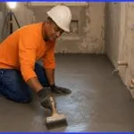 Pedreiro profissional aplicando argamassa polimérica em banheiro de apartamento em Salvador durante reforma residencial com impermeabilização conforme NBR 9575